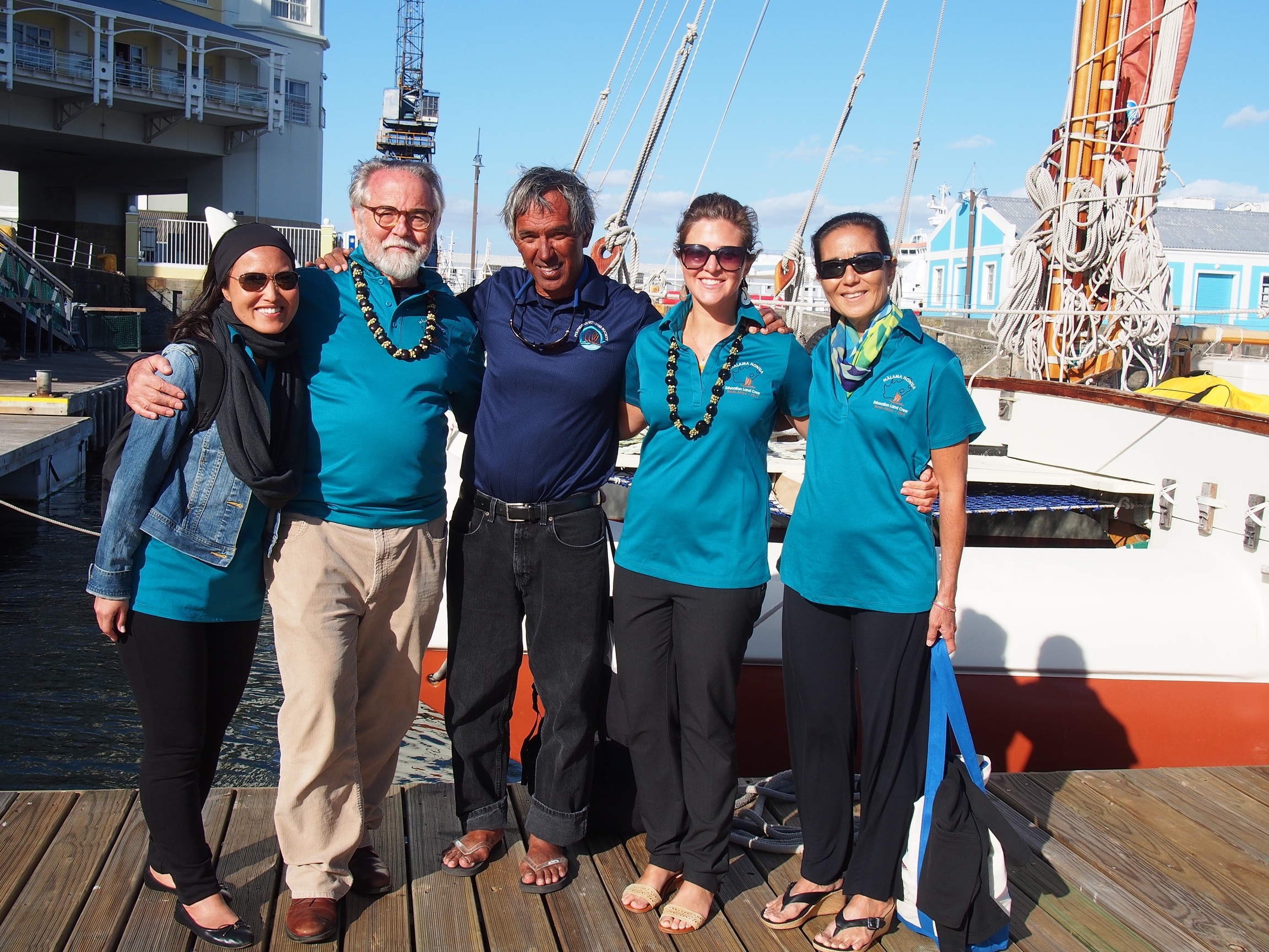 Mālama Honua Education Land Crew members Megan Kawatachi, Robert Witt, Michelle Knoetgen, and Diane Tom-Ogata stand with Caption Nainoa Thompson in front of Hōkūle'a in Cape Town Harbor after the Hōkūle'a Arrival Ceremony. 