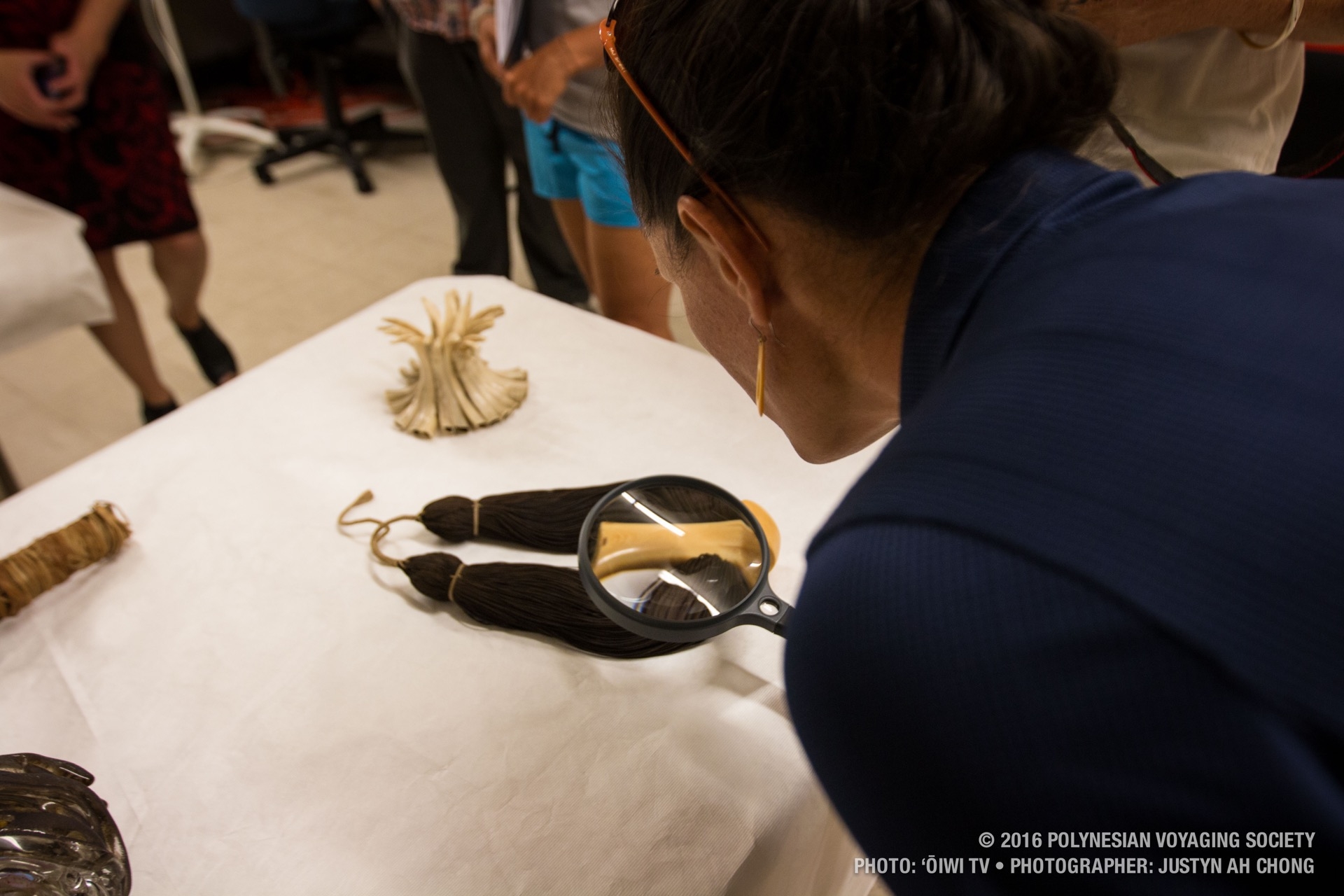 Kaʻiulani Murphy inspects the intricacies of a lei niho palaoa through a magnifying glass.